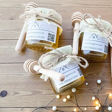 Four small jars of honey with dipper sticks on a wooden surface with string lights.