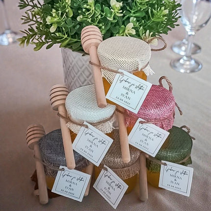 Decorative honey jars with wooden spoons on a table with a plant in the background