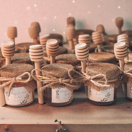 Jars of honey with wooden dipper handles on a wooden surface.