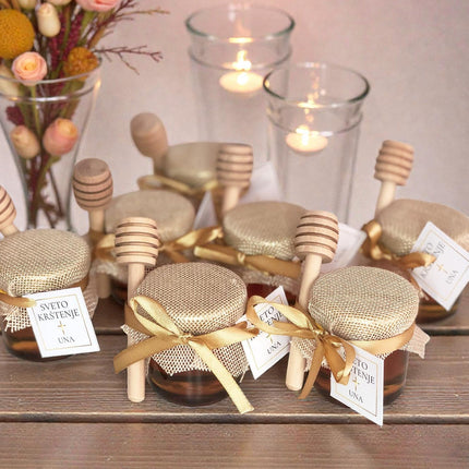 Jars of honey with dipper sticks on a wooden surface, accompanied by flowers and candles.
