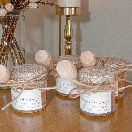 Decorative jars with burlap bows on a wooden surface, with a candle and flowers in the background.