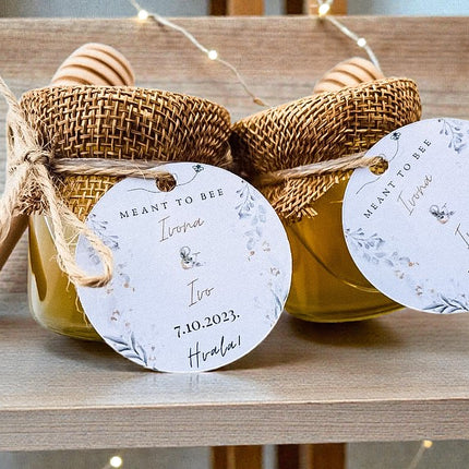 Two jars of honey with burlap wrapping and personalized tags on a wooden surface.