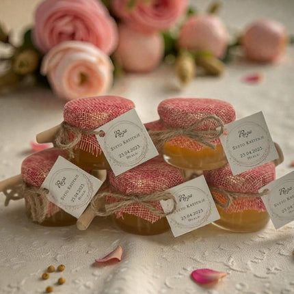 Jars of honey with decorative lids and tags, surrounded by pink flowers on a light background